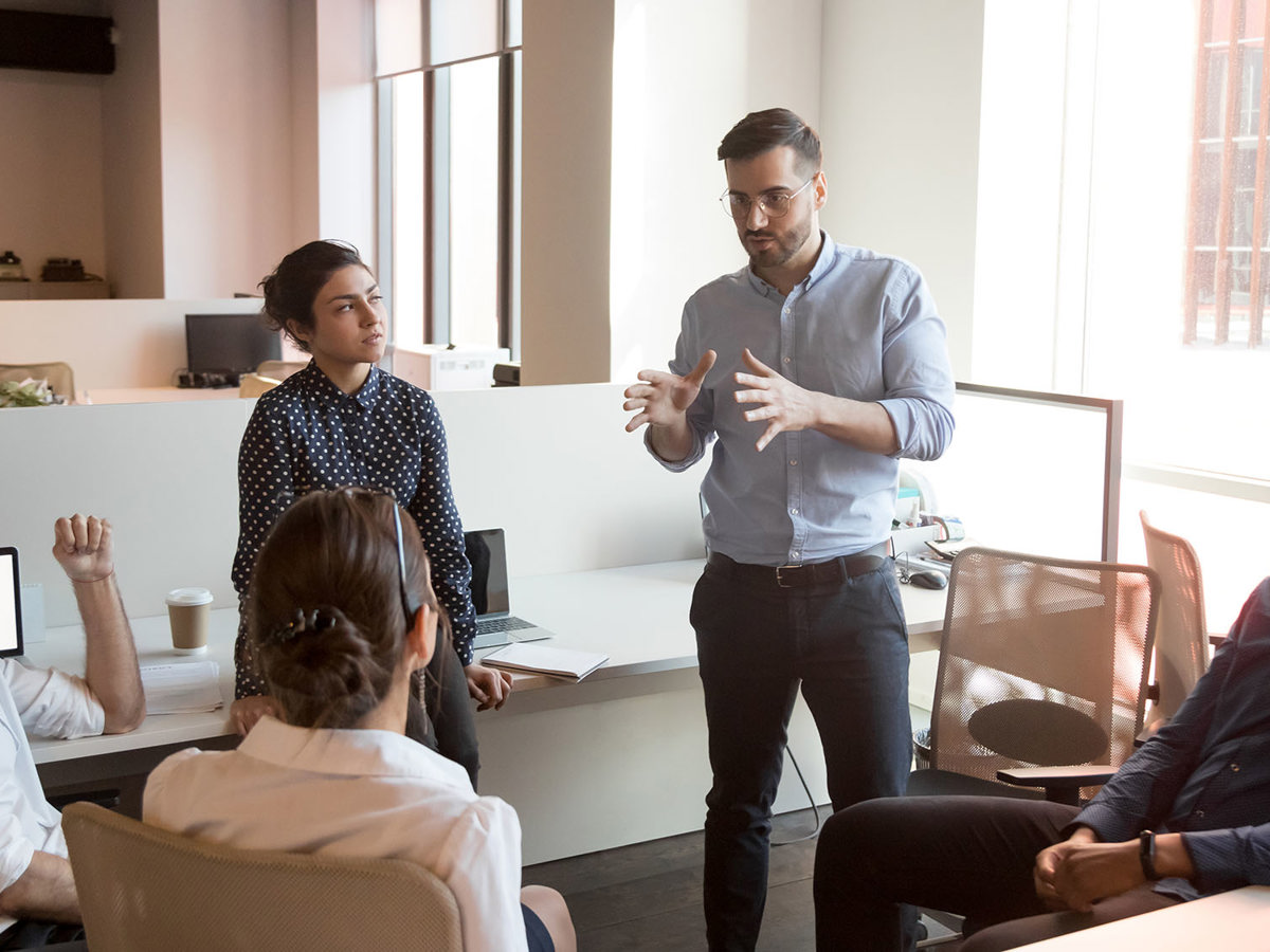 training man standing talking to 4 sitting others