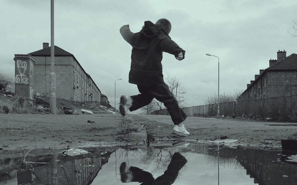 Black and white photo of child jumping over puddle