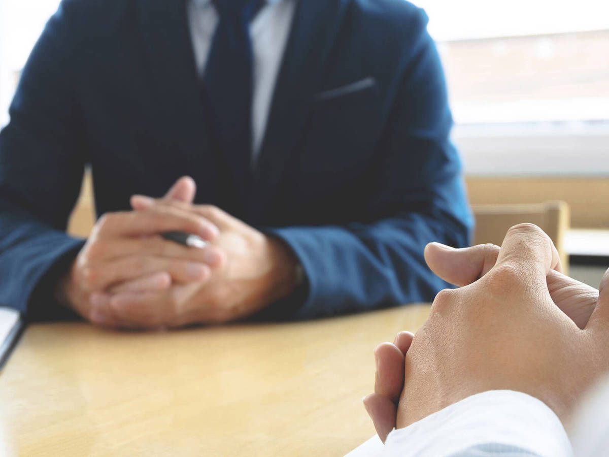 man with his hands clenched together sitting at a meeting