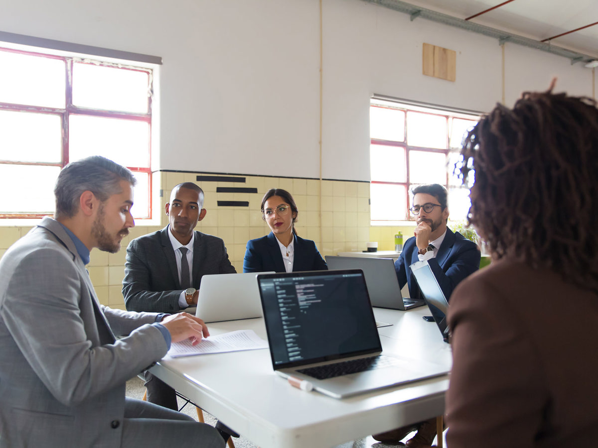 training group of five professionals sitting at a table with laptops